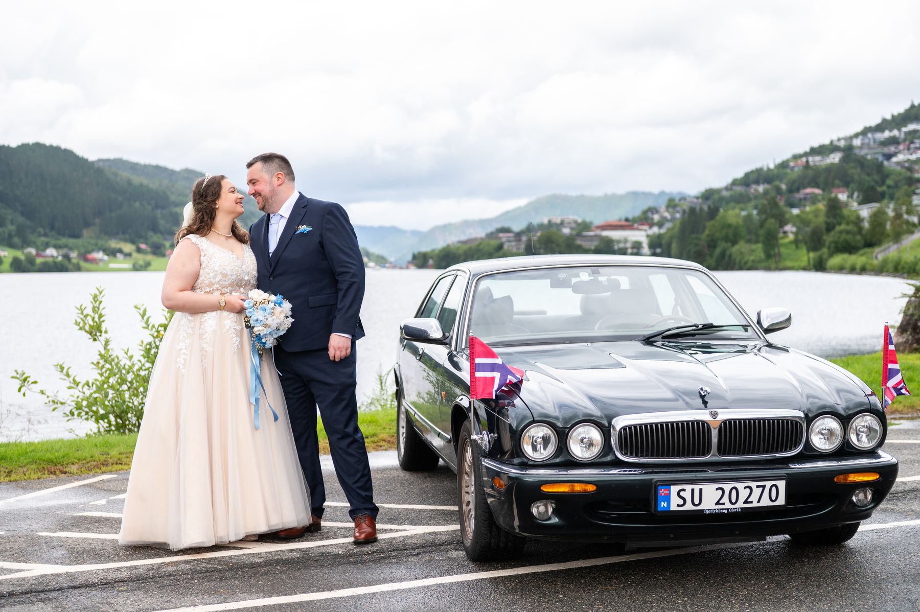 Brudepar ved Jaguar XJ i British Racing Green, med norsk og britisk flagg på skjermene og fjorden i bakgrunnen